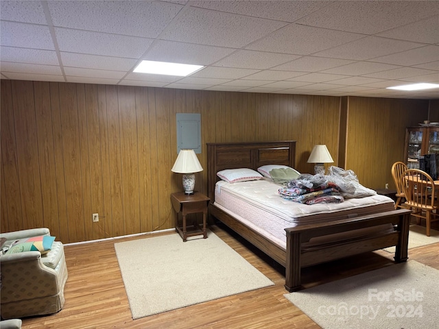 bedroom featuring a paneled ceiling, wood walls, and hardwood / wood-style floors