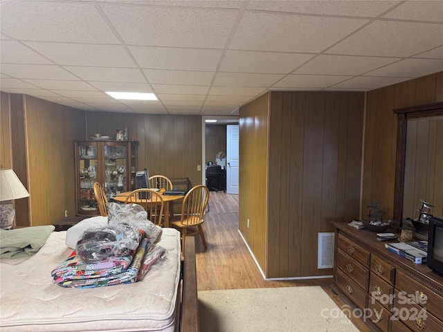 bedroom featuring a paneled ceiling, wooden walls, and hardwood / wood-style floors