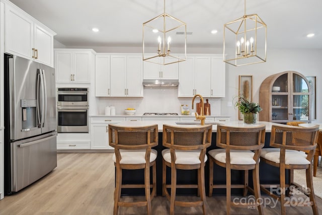 kitchen featuring stainless steel appliances, hanging light fixtures, a center island with sink, and light hardwood / wood-style floors