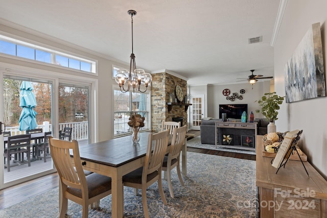 dining room featuring a stone fireplace, crown molding, wood-type flooring, a textured ceiling, and ceiling fan with notable chandelier