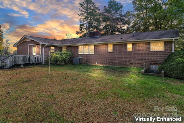 back house at dusk with a lawn, central air condition unit, and a wooden deck