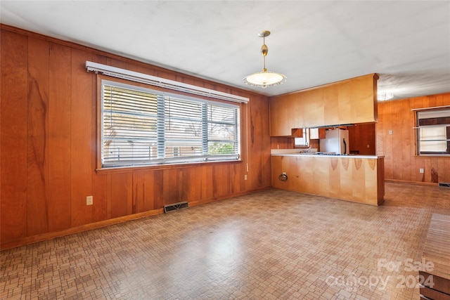 kitchen featuring kitchen peninsula, stainless steel fridge, pendant lighting, and wood walls