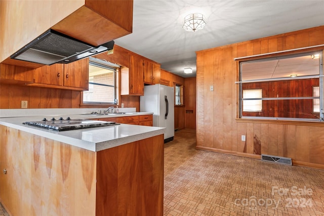 kitchen with kitchen peninsula, white refrigerator, stainless steel gas cooktop, and wooden walls