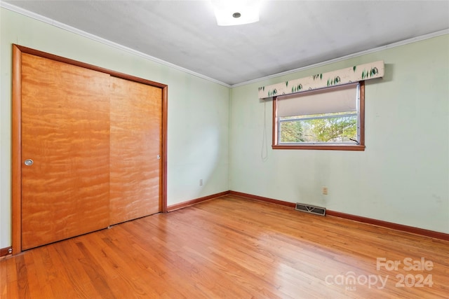 unfurnished bedroom featuring a closet, ornamental molding, and hardwood / wood-style flooring