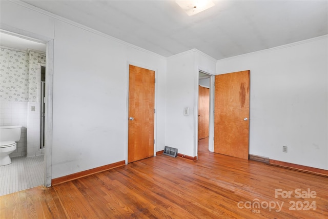 unfurnished bedroom with hardwood / wood-style floors, ensuite bathroom, tile walls, and crown molding