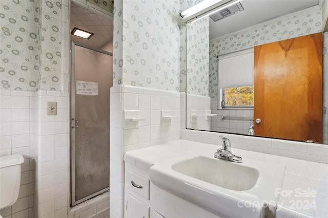 bathroom with an enclosed shower, vanity, toilet, and tile walls