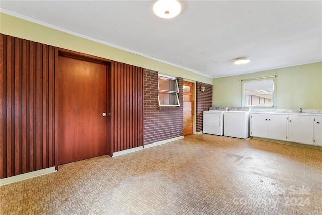 clothes washing area with cabinets, ornamental molding, brick wall, sink, and washing machine and dryer