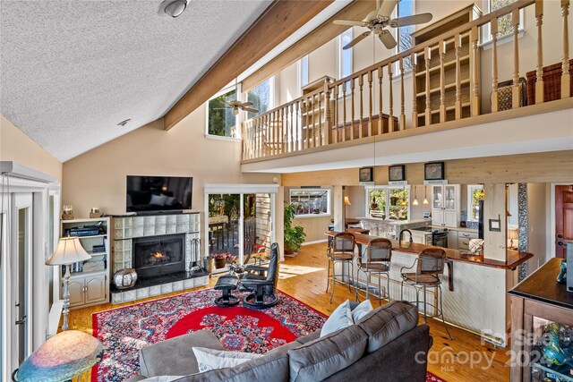 living room with hardwood / wood-style flooring, high vaulted ceiling, plenty of natural light, and a tiled fireplace