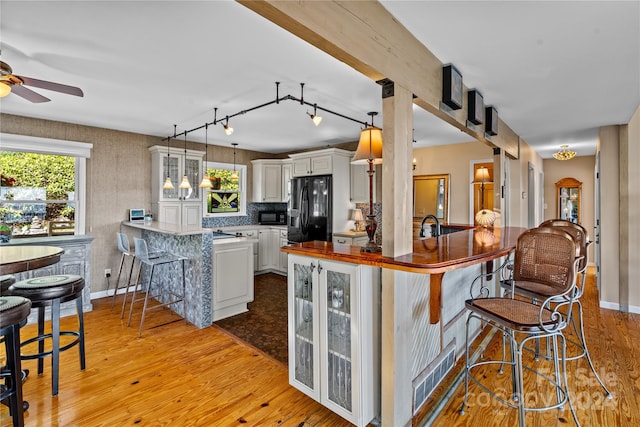 kitchen featuring kitchen peninsula, light hardwood / wood-style flooring, white cabinets, and black appliances