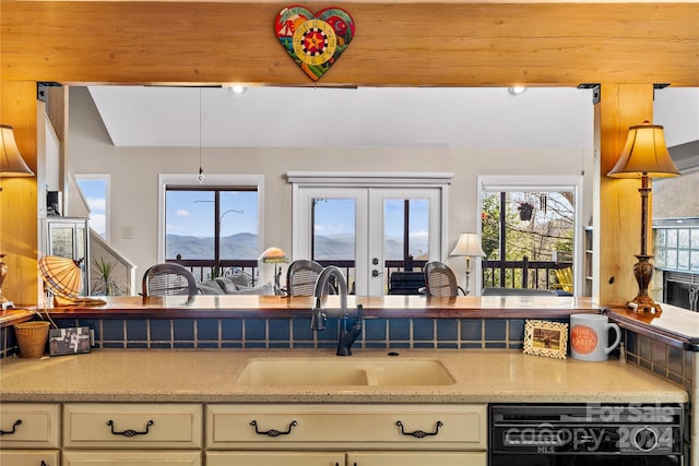 kitchen with a mountain view, black dishwasher, light stone countertops, and sink