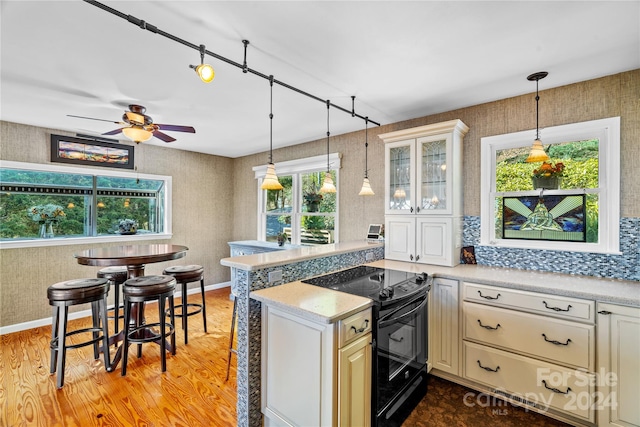 kitchen with black range with electric stovetop, ceiling fan, light stone countertops, pendant lighting, and light wood-type flooring