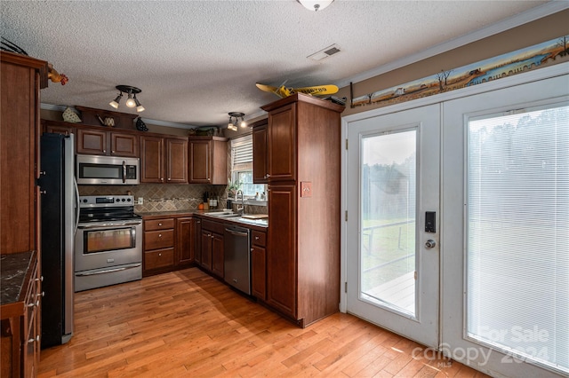 kitchen with backsplash, sink, ornamental molding, light hardwood / wood-style floors, and stainless steel appliances