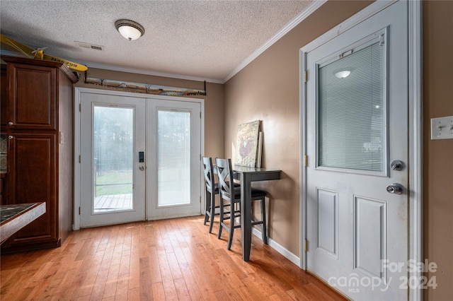 doorway to outside with french doors, a textured ceiling, light hardwood / wood-style floors, and ornamental molding