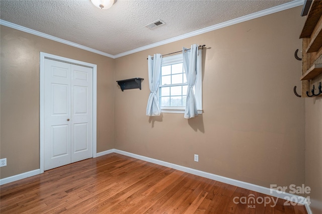 unfurnished bedroom featuring crown molding, a closet, a textured ceiling, and hardwood / wood-style flooring