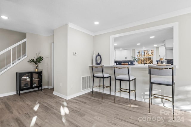 kitchen featuring kitchen peninsula, a kitchen breakfast bar, crown molding, white cabinets, and light hardwood / wood-style floors