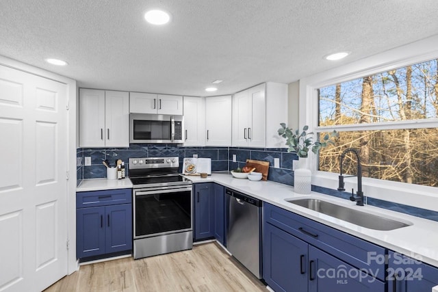 kitchen with blue cabinetry, sink, light hardwood / wood-style flooring, white cabinets, and appliances with stainless steel finishes