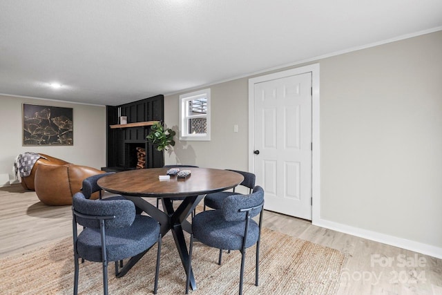 dining space featuring a fireplace, light wood-type flooring, and ornamental molding