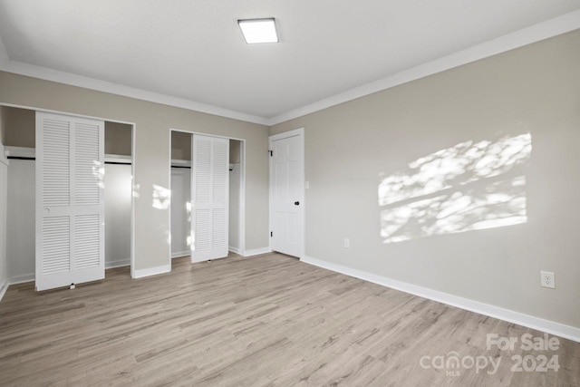 unfurnished bedroom with light wood-type flooring, crown molding, and multiple closets