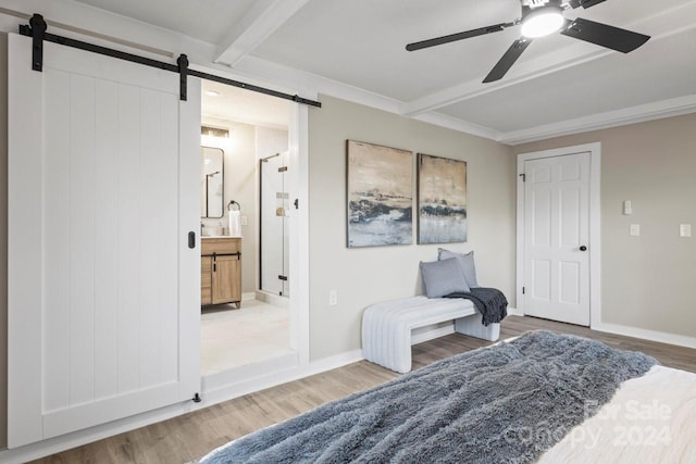 bedroom with beam ceiling, ceiling fan, a barn door, ensuite bathroom, and wood-type flooring