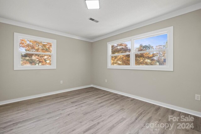 spare room featuring plenty of natural light, light wood-type flooring, and crown molding