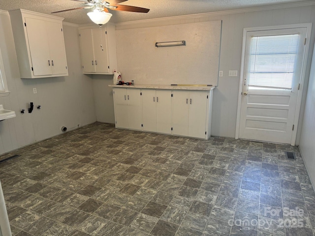 laundry room featuring ceiling fan, cabinets, ornamental molding, and a textured ceiling