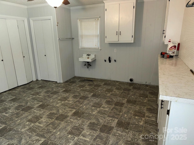 clothes washing area with ceiling fan, sink, a textured ceiling, wooden walls, and ornamental molding