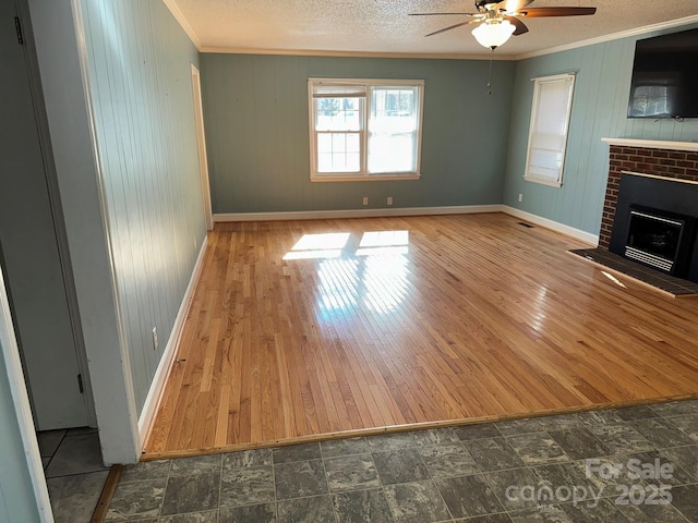 unfurnished living room with ceiling fan, crown molding, wooden walls, and a brick fireplace