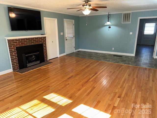 unfurnished living room featuring a brick fireplace, a textured ceiling, ceiling fan, crown molding, and dark hardwood / wood-style floors