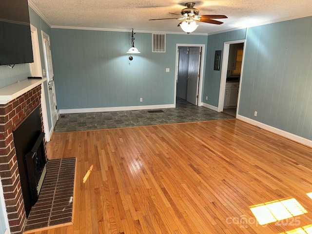 unfurnished living room with hardwood / wood-style flooring, ornamental molding, a textured ceiling, and wooden walls