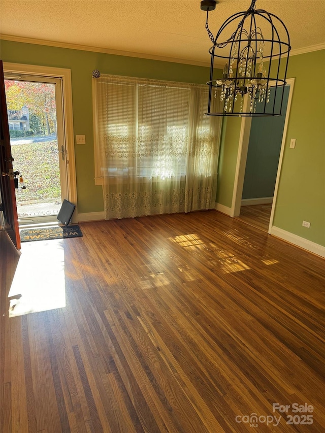 unfurnished dining area featuring a textured ceiling, dark hardwood / wood-style flooring, an inviting chandelier, and ornamental molding