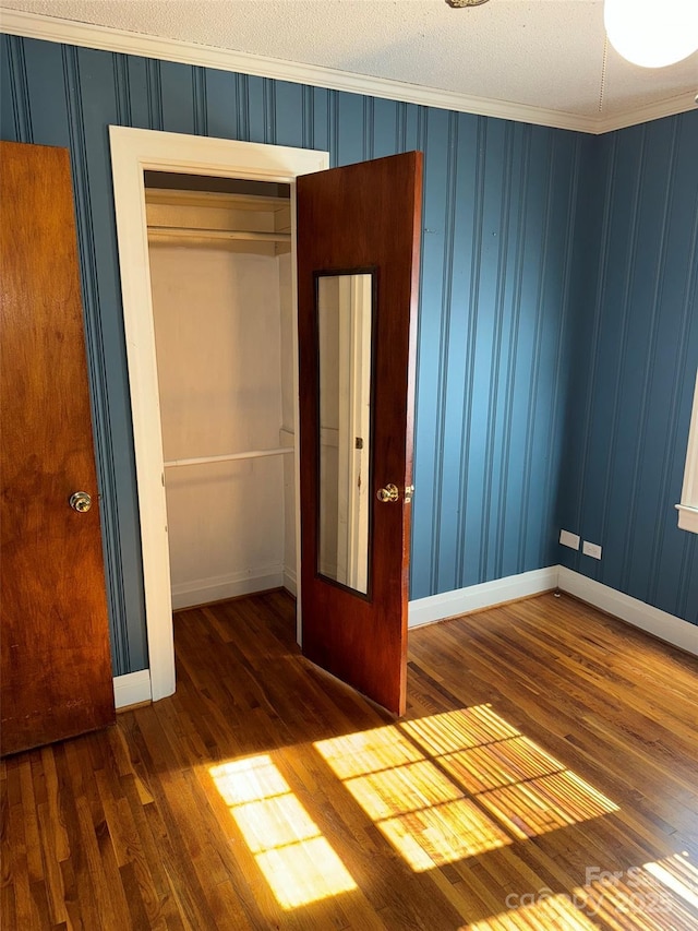 unfurnished bedroom featuring dark hardwood / wood-style floors, ornamental molding, a textured ceiling, and a closet