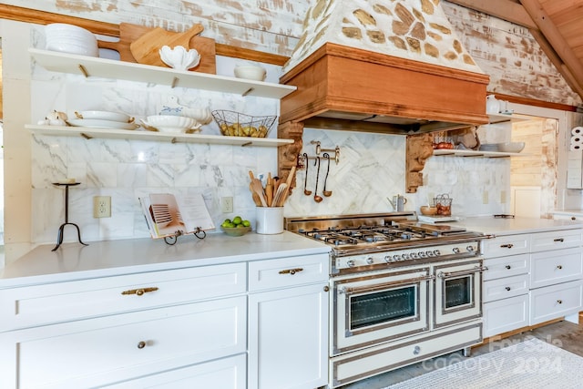 kitchen featuring double oven range, premium range hood, vaulted ceiling, tasteful backsplash, and white cabinetry