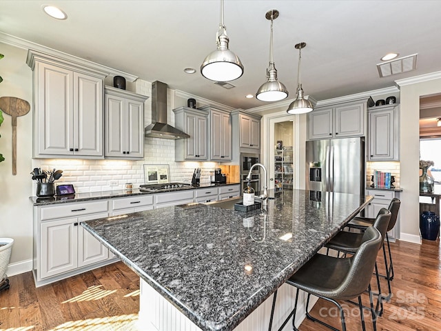 kitchen featuring a breakfast bar, a large island with sink, wall chimney exhaust hood, dark hardwood / wood-style flooring, and stainless steel appliances