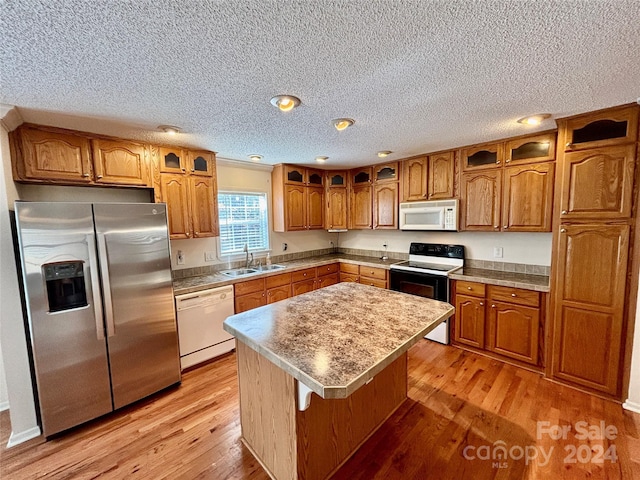 kitchen featuring sink, a center island, light hardwood / wood-style flooring, a textured ceiling, and white appliances