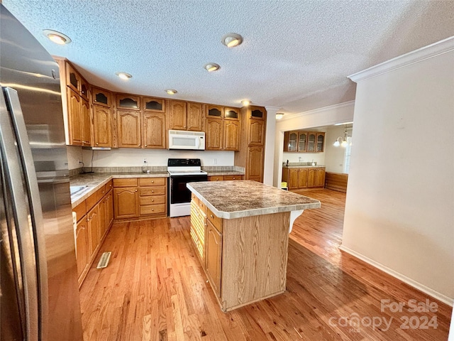 kitchen featuring a center island, light hardwood / wood-style floors, a textured ceiling, white appliances, and ornamental molding