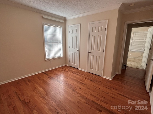 unfurnished bedroom with hardwood / wood-style floors, a textured ceiling, crown molding, and multiple closets