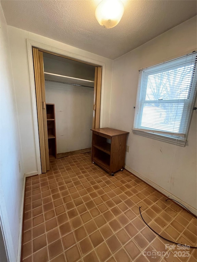 unfurnished bedroom featuring a closet, a textured ceiling, and baseboards