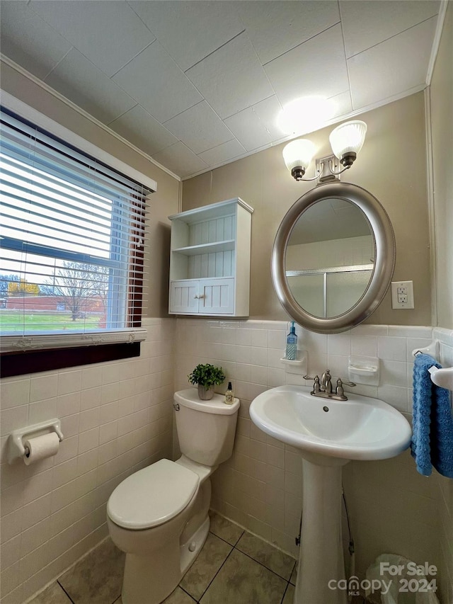 bathroom with toilet, tile patterned floors, and tile walls