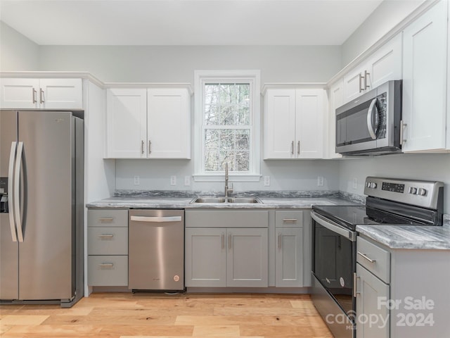 kitchen featuring sink, light stone countertops, light wood-type flooring, white cabinetry, and stainless steel appliances