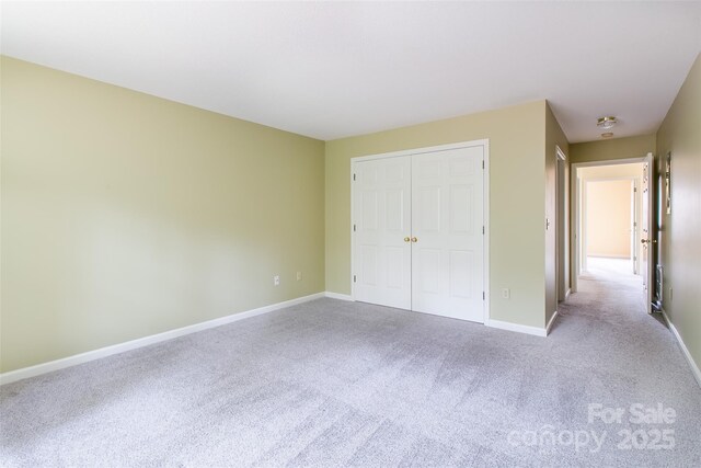 unfurnished bedroom with a closet, light colored carpet, and baseboards