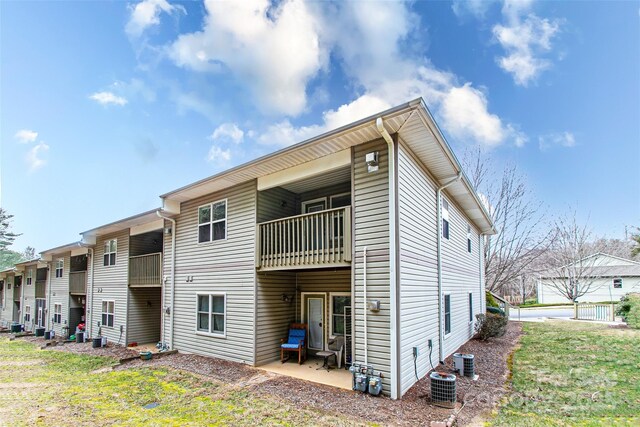 back of house featuring a balcony, central AC unit, and a lawn