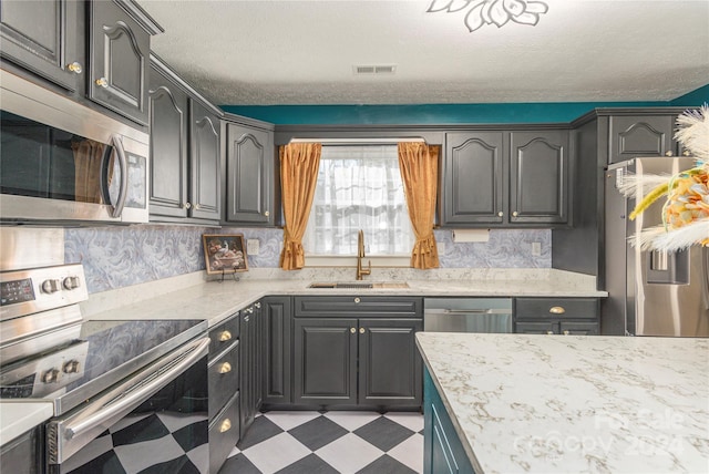 kitchen with backsplash, light stone counters, a textured ceiling, stainless steel appliances, and sink