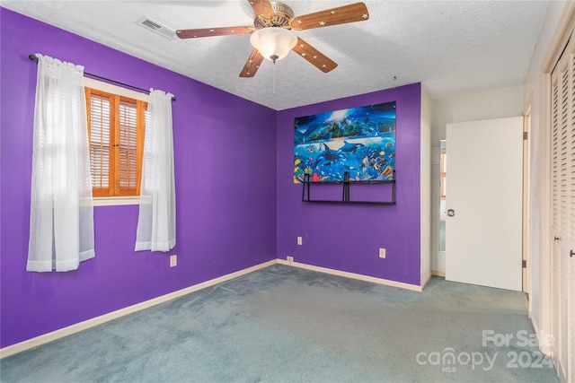 carpeted spare room featuring a textured ceiling and ceiling fan