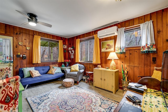 living area with light hardwood / wood-style floors, an AC wall unit, ceiling fan, and wooden walls