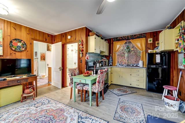 kitchen featuring wood walls, electric range oven, black fridge, ceiling fan, and light hardwood / wood-style floors