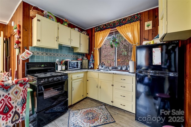 kitchen with tasteful backsplash, sink, black appliances, cream cabinets, and light hardwood / wood-style floors