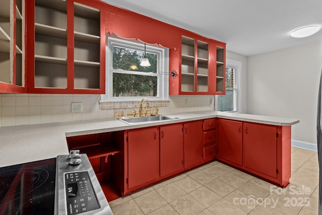 kitchen with backsplash, range, sink, light tile patterned flooring, and kitchen peninsula