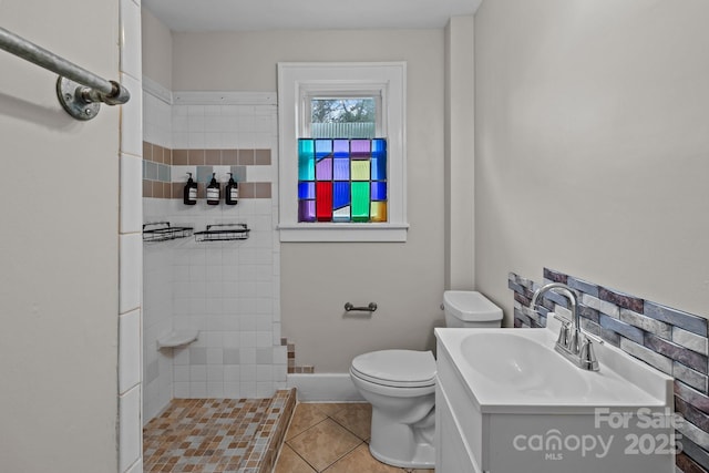 bathroom with tile patterned floors, vanity, toilet, and a tile shower