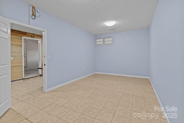 tiled empty room with a textured ceiling and wooden walls