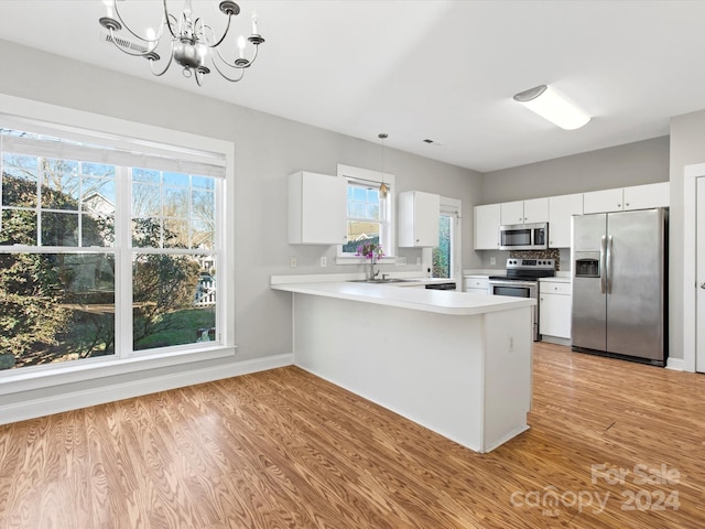 kitchen with white cabinets, pendant lighting, light wood-type flooring, and stainless steel appliances